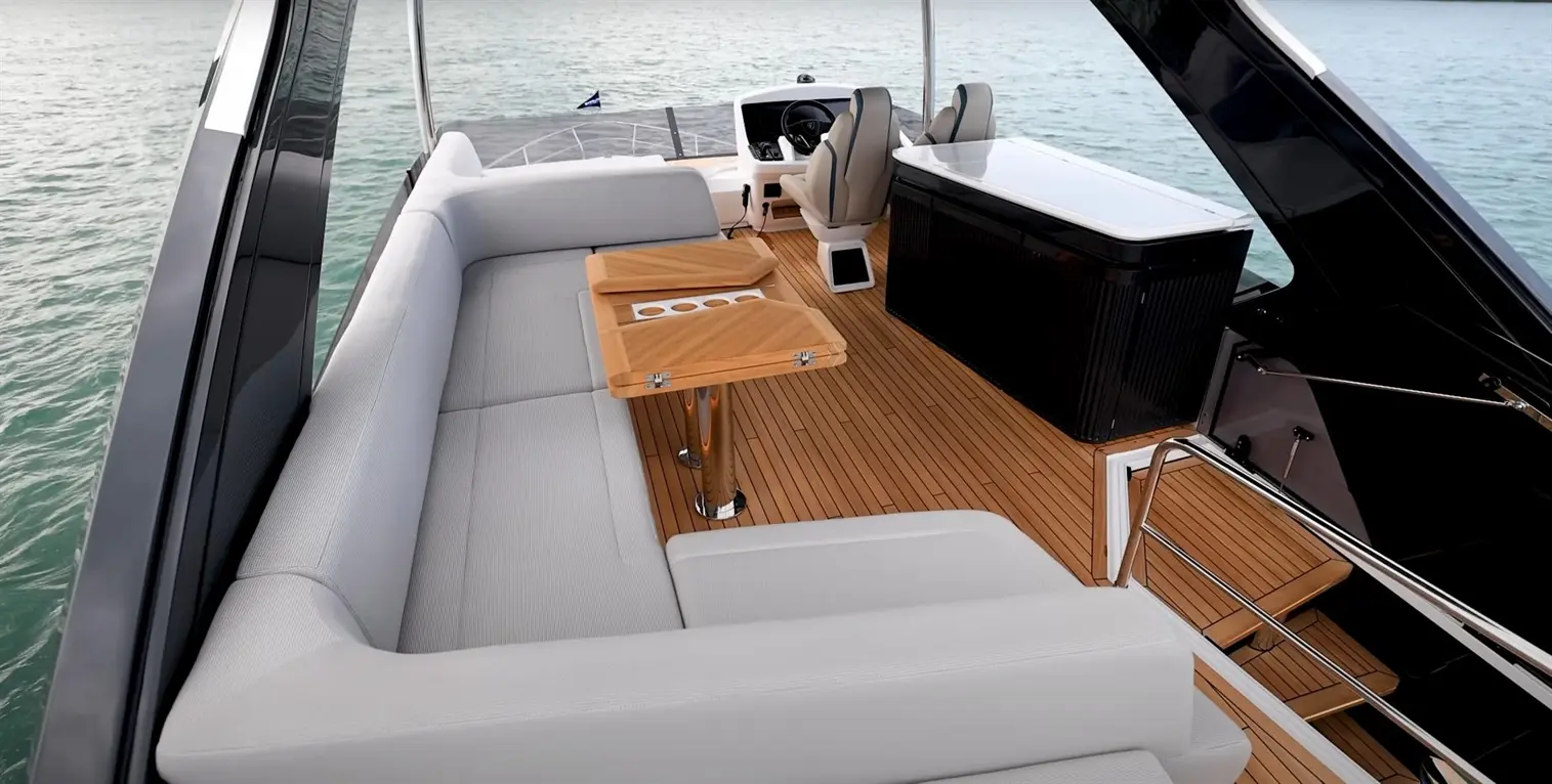 Luxury boat interior featuring grey seating, wooden tables, and a bar area, with a scenic water view in the background.